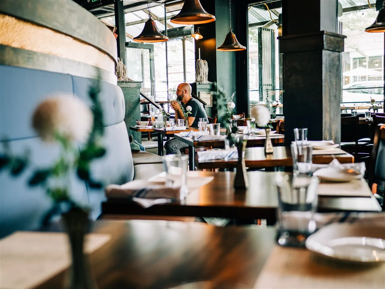 Grappa's dining room in Queen Anne with wooden tables, a blue banquette, copper pendant lights and tall windows
