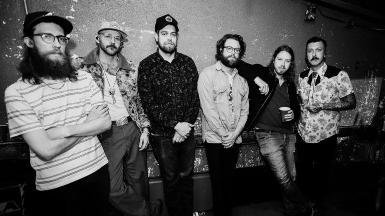 Black and white photo of the six members of American Aquarium standing against a weathered, peeling wall, ahead of their show at The Crocodile near Grappa