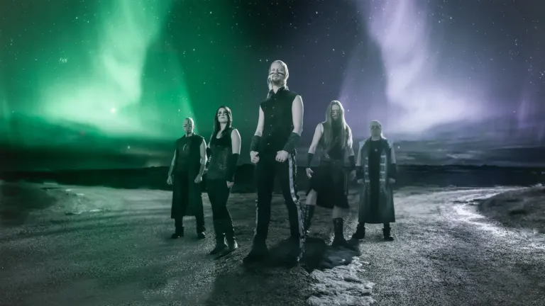 The five members of Ensiferum in dark stage clothes standing on a rocky road under green and purple northern lights, ahead of their El Corazon show near Grappa