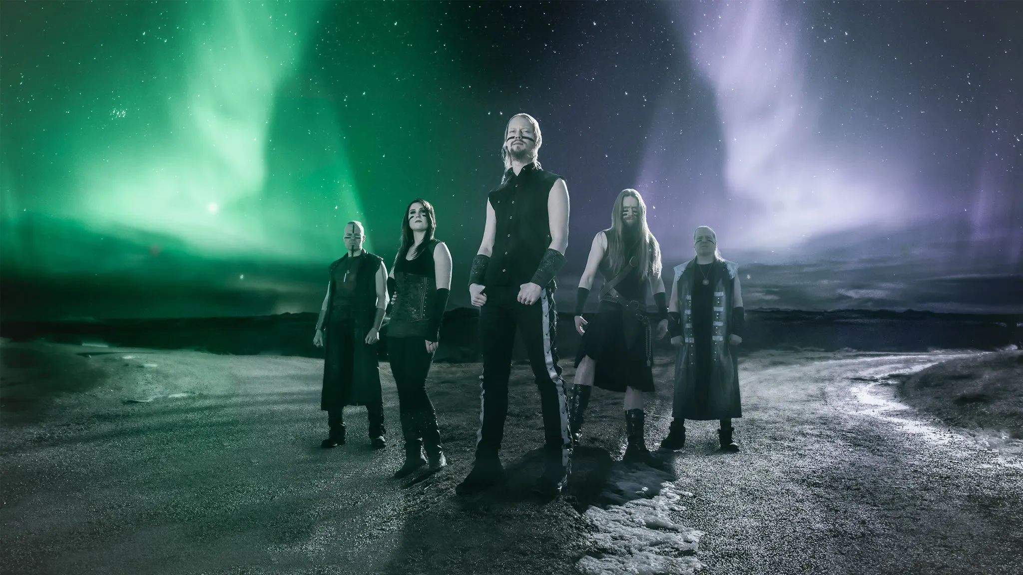 The five members of Ensiferum in dark stage clothes standing on a rocky road under green and purple northern lights, ahead of their El Corazon show near Grappa