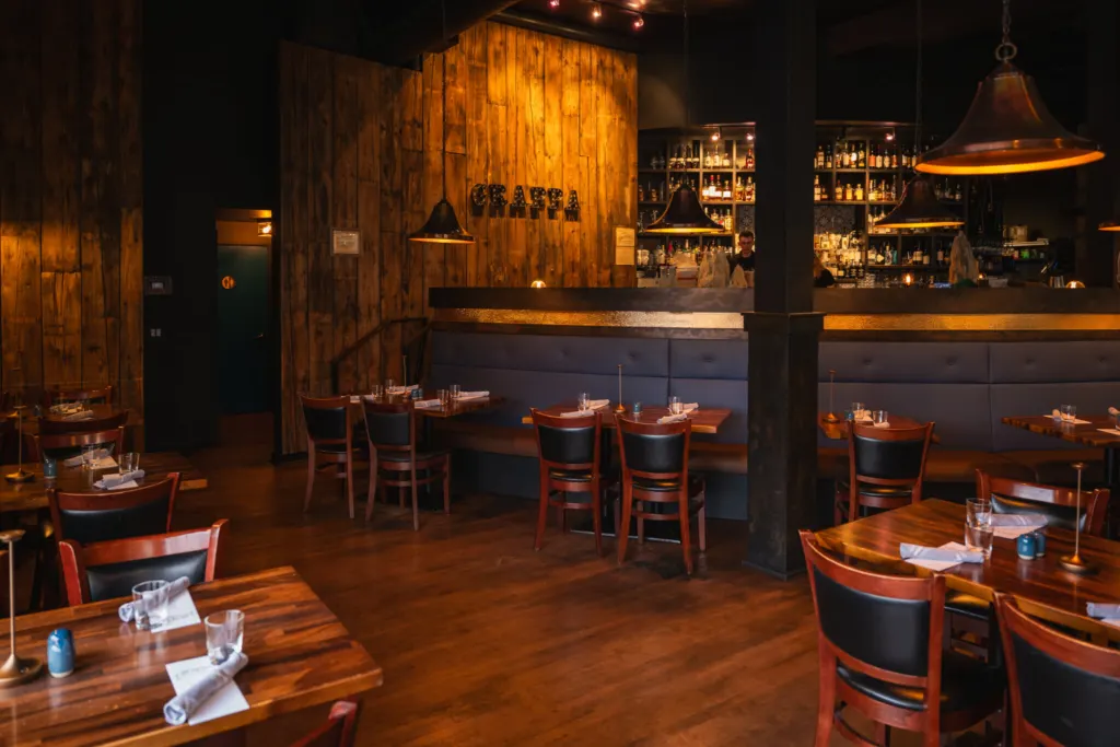 Grappa's dining room in Queen Anne with wooden tables, leather chairs, a blue banquette, the Grappa sign on a wood wall and the bar behind