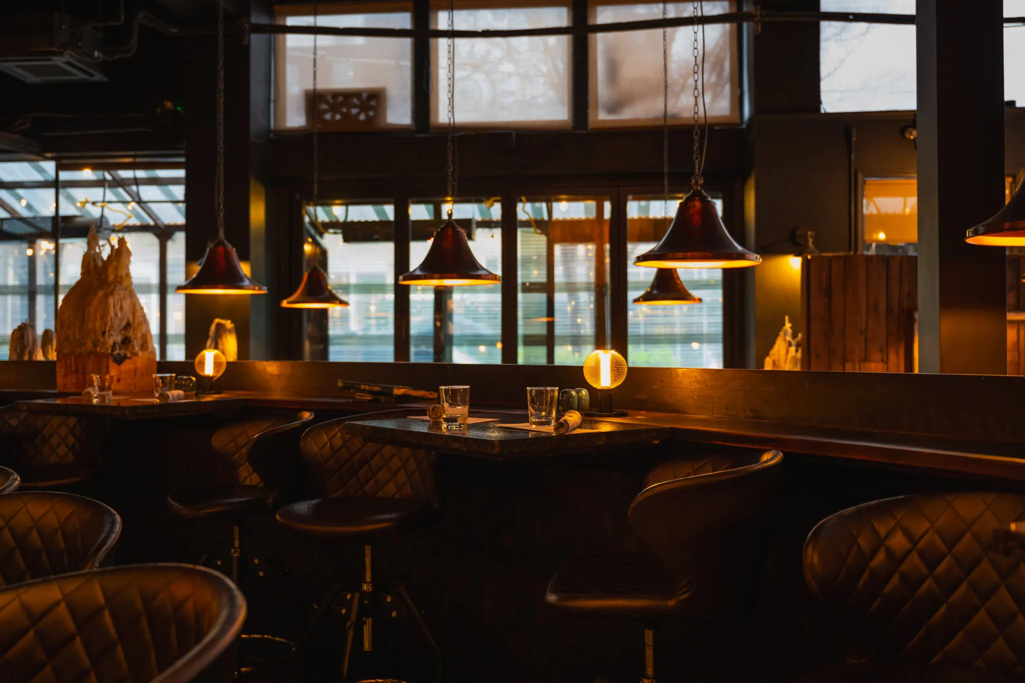 Grappa's bar area in Queen Anne at dusk with high-top tables, quilted leather bar stools, copper pendant lamps and tall windows