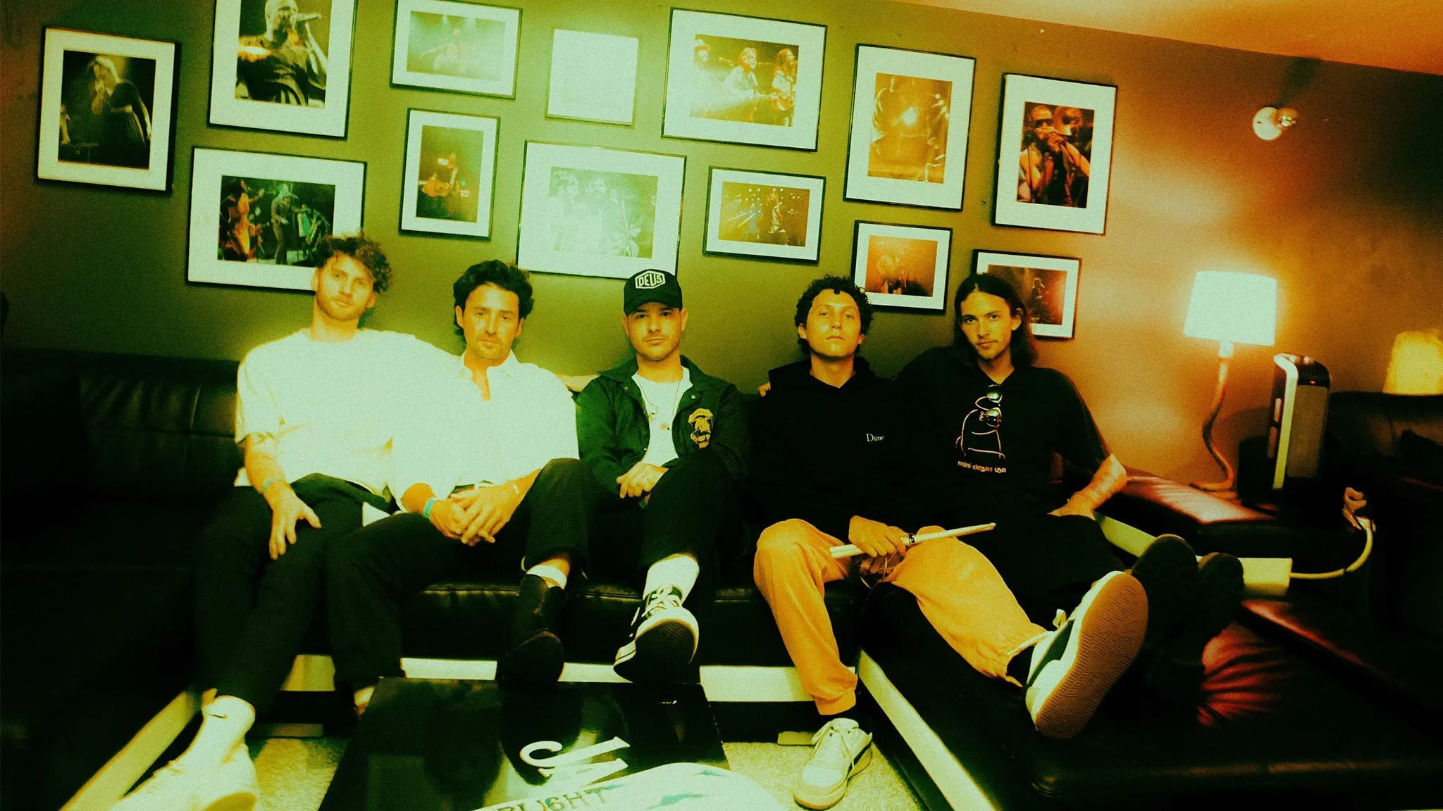 Stop Light Observations relaxing on a black leather couch under a wall of framed concert photos, ahead of their Hidden Hall show near Grappa