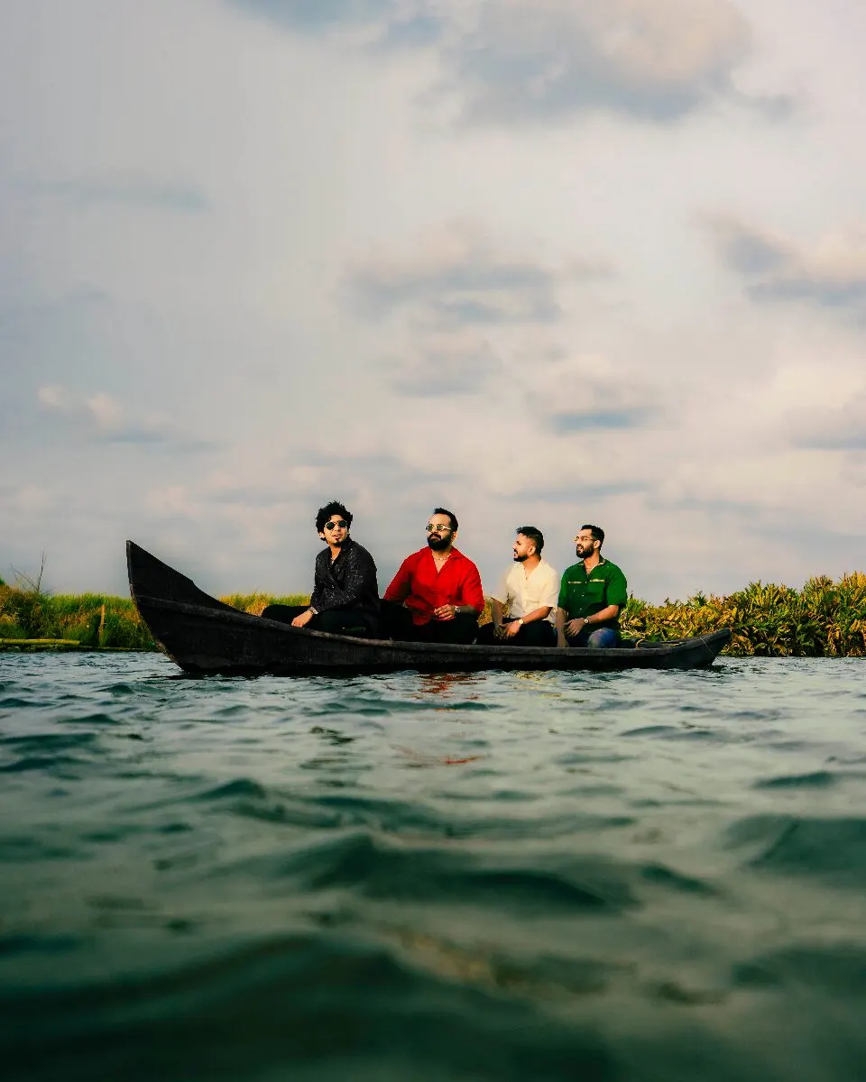 The four members of When Chai Met Toast sitting in a long wooden boat on open water under a cloudy sky, ahead of their Fremont Abbey show near Grappa in Queen Anne